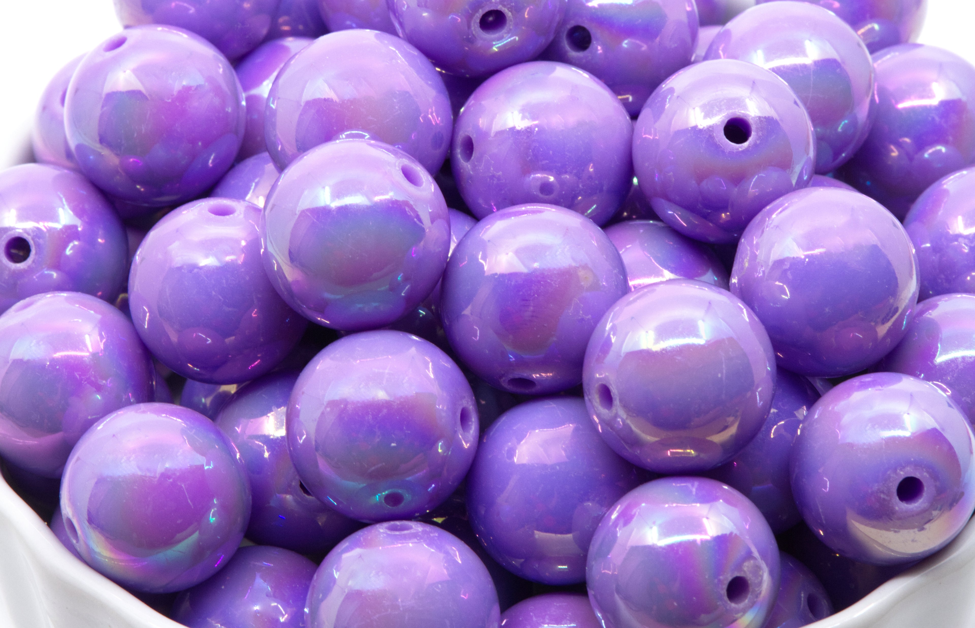 Purple iridescent beads in a white bowl on a white background