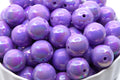 Purple iridescent beads in a white bowl on a white background