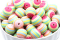 A pile of round, pastel-striped beads in a white bowl. The beads feature horizontal stripes of pink, light blue, mint green, yellow, and peach, and pink.