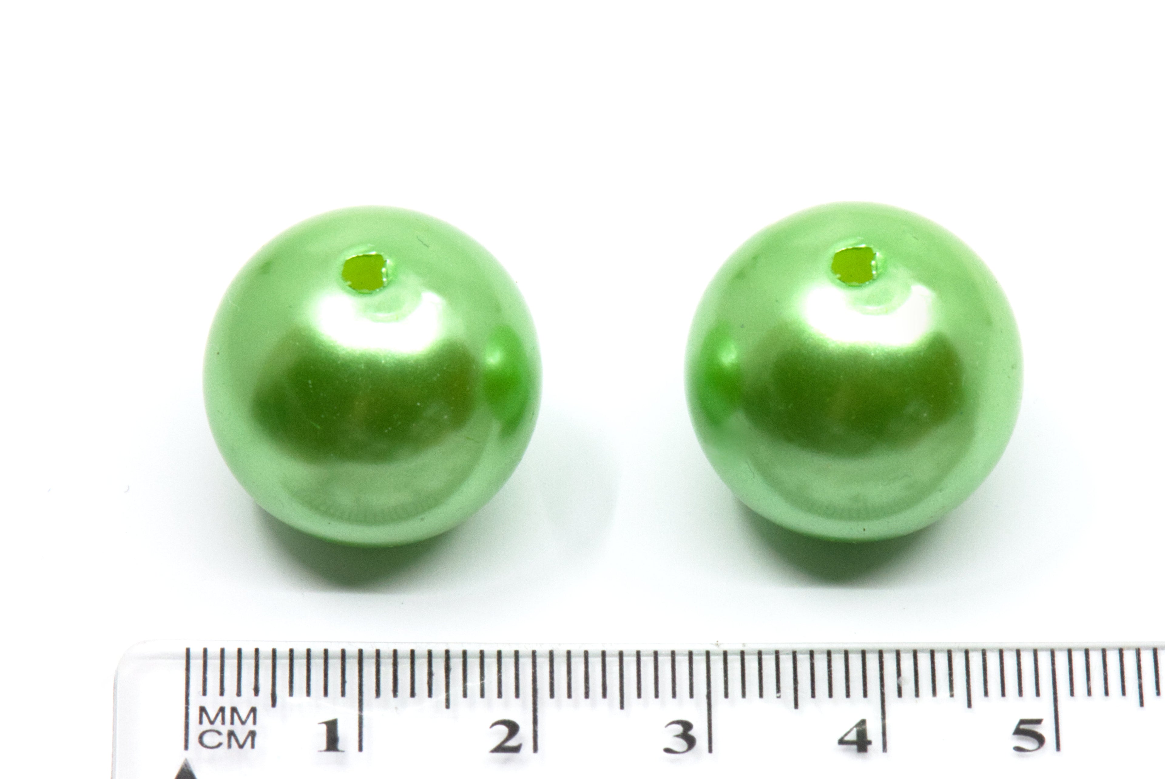 Two green metallic beads next to a ruler for size reference on a white background