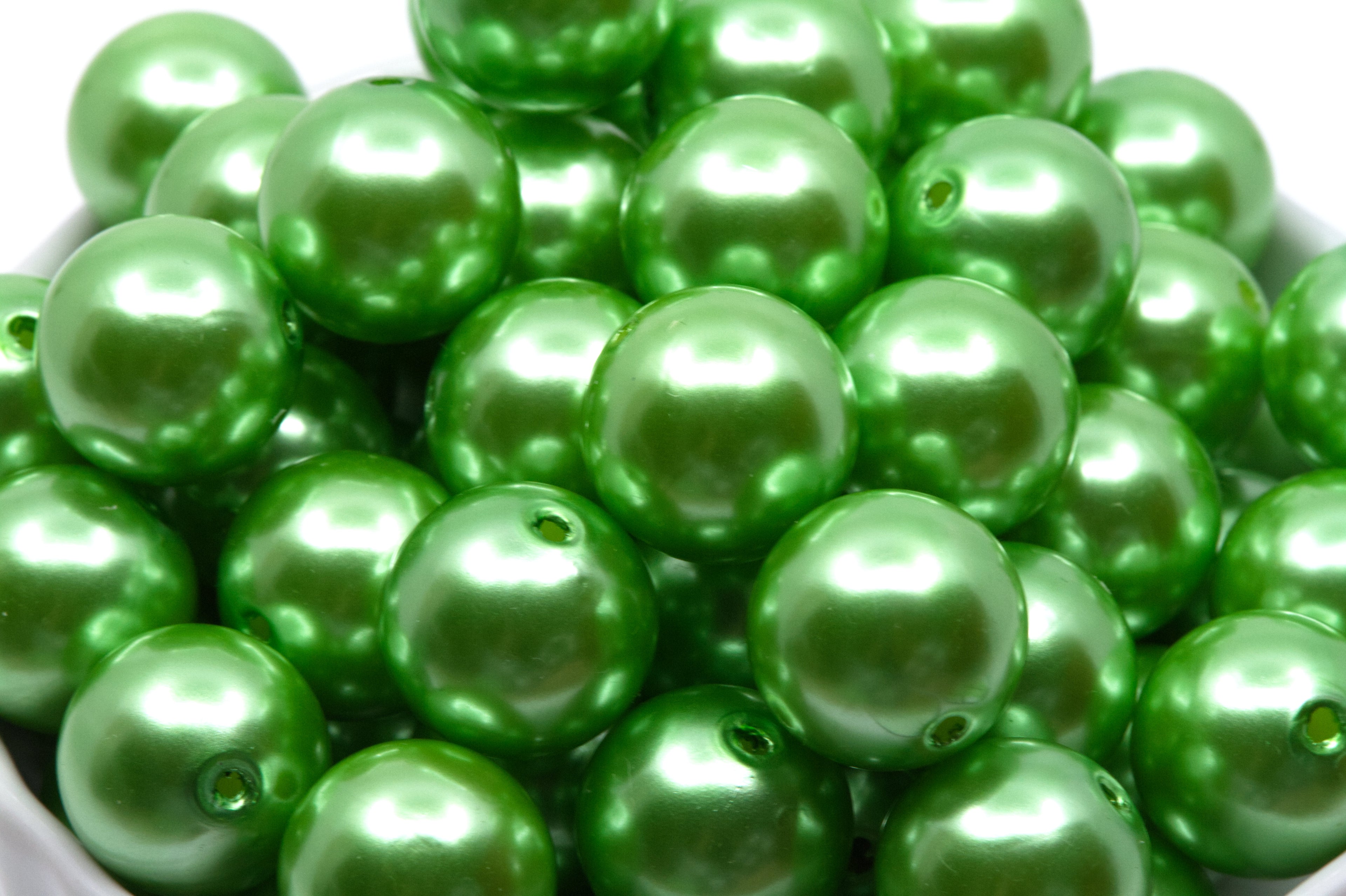 Green metallic beads in a white bowl on a white background 