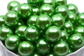 Green metallic beads in a white bowl on a white background