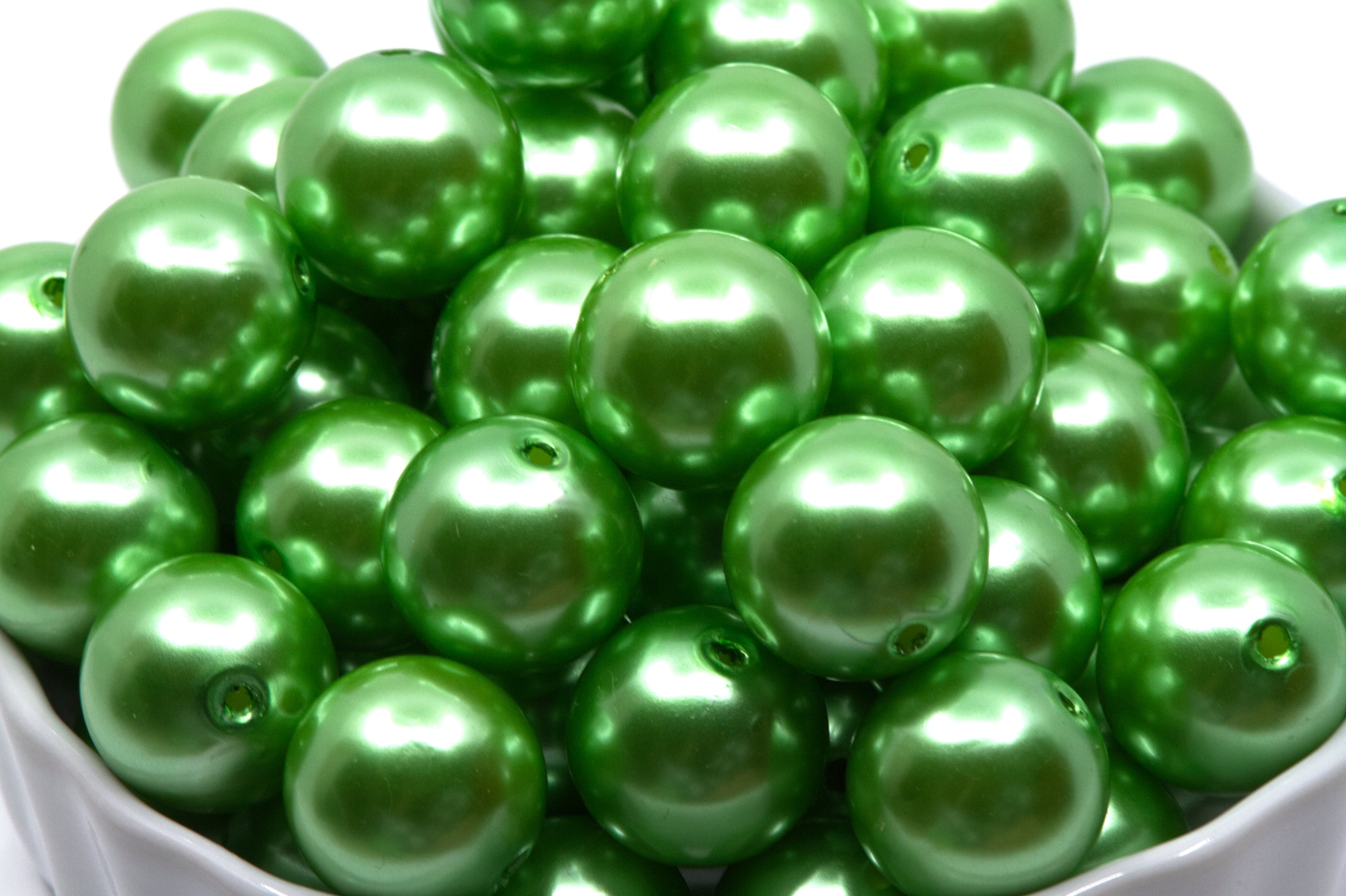 Green metallic beads in a white bowl on a white background