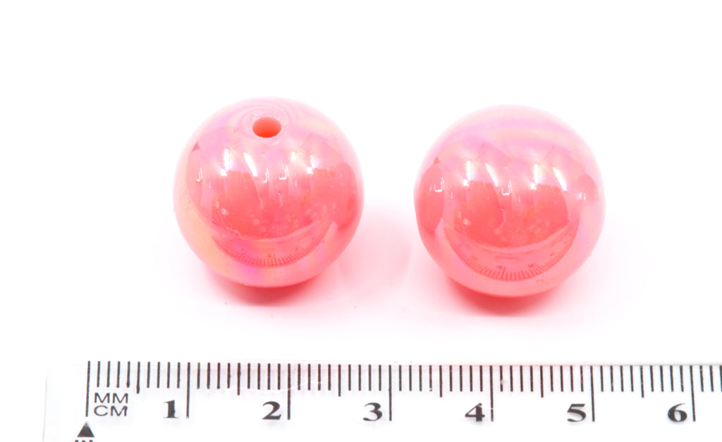 Two pink beads with a ruler for scale on a white background