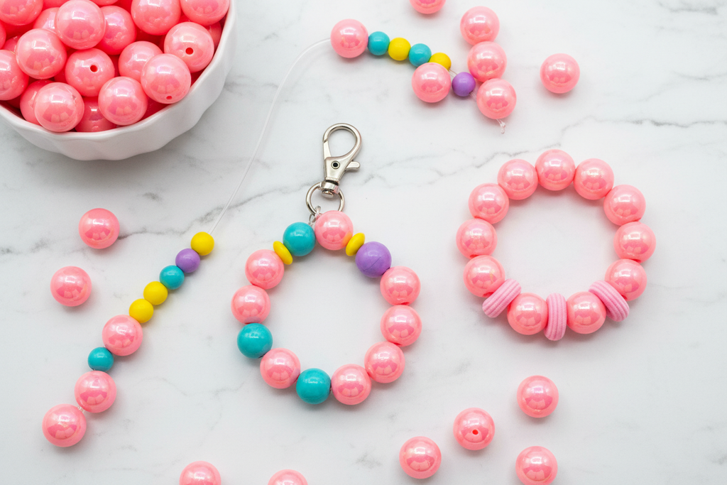 Pink bead shown in accessories including a bracelet, keychain, and keyring on a marble surface.