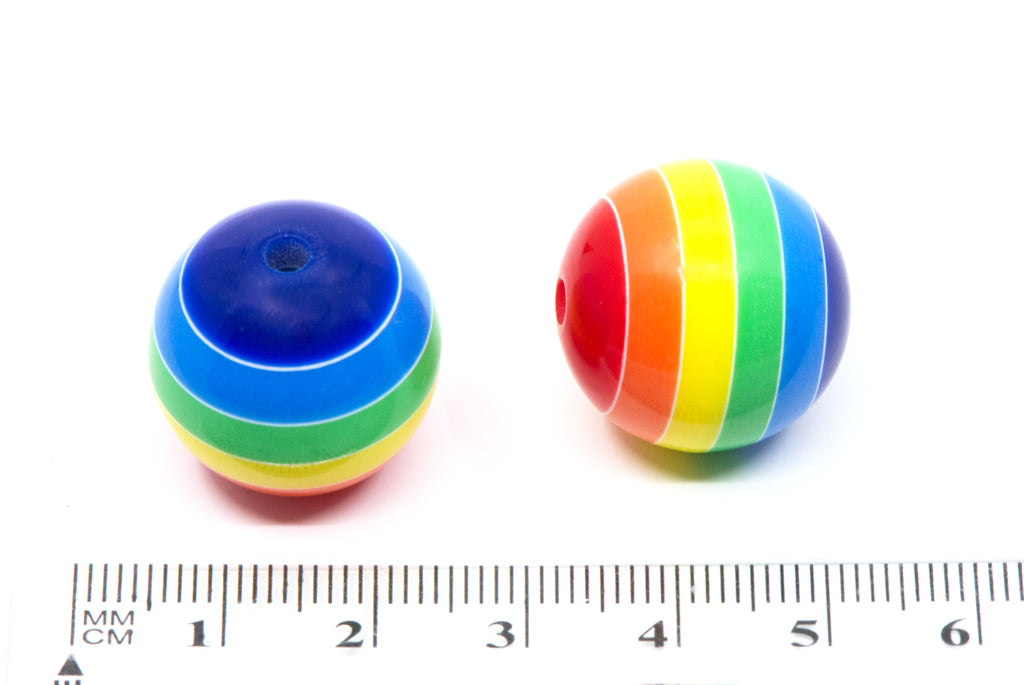 Two small rainbow-striped spherical beads shown on a white background with a ruler at the bottom for scale.