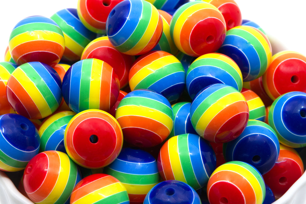 A pile of rainbow striped bubblegum beads, shown close-up in a white container against a white background.