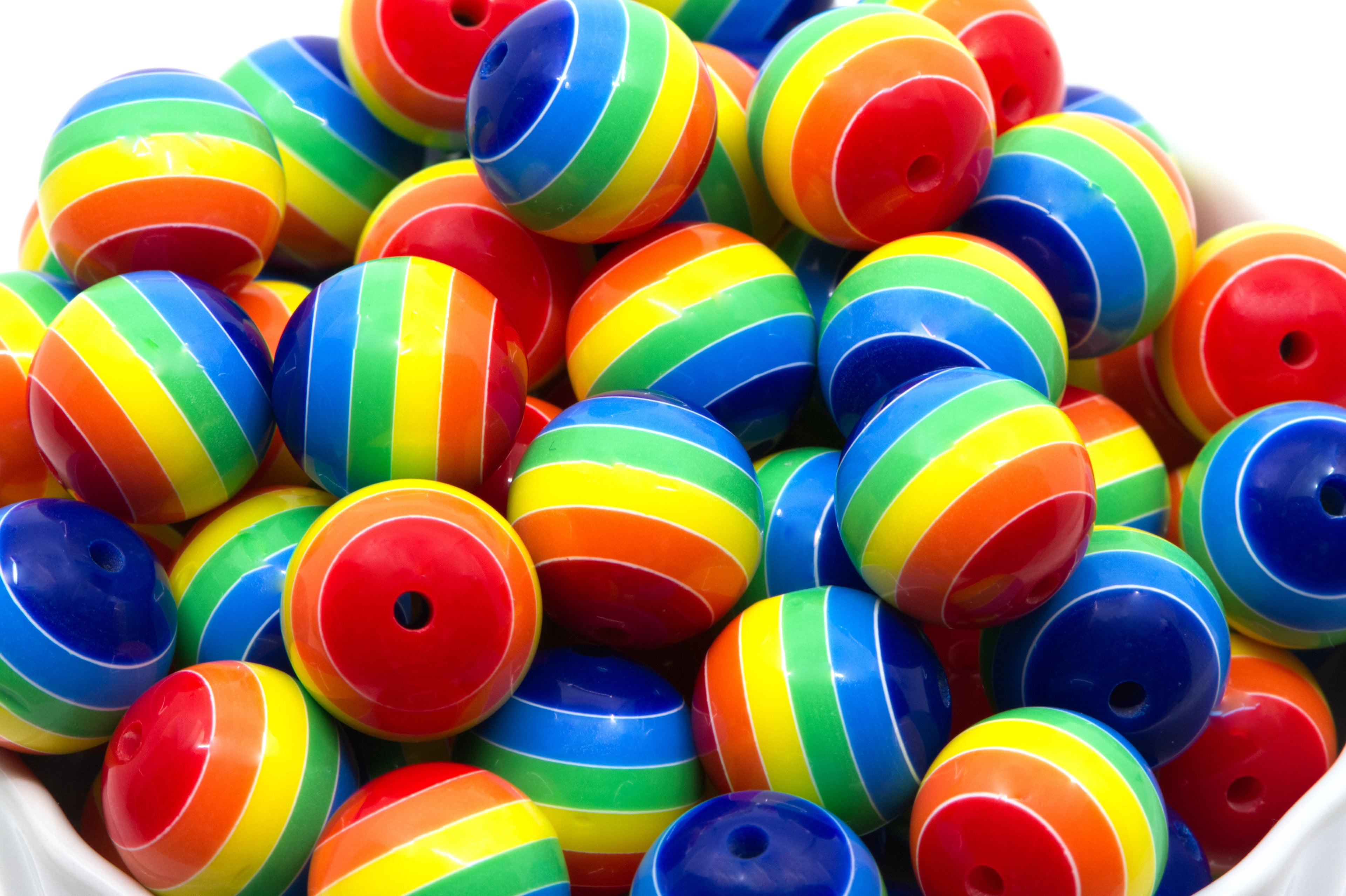 A pile of rainbow striped bubblegum beads, shown close-up in a white container against a white background.
