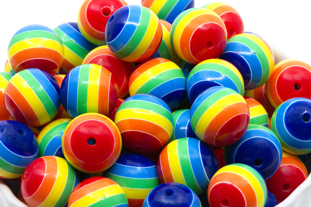 A pile of rainbow striped bubblegum beads, shown close-up in a white container against a white background.