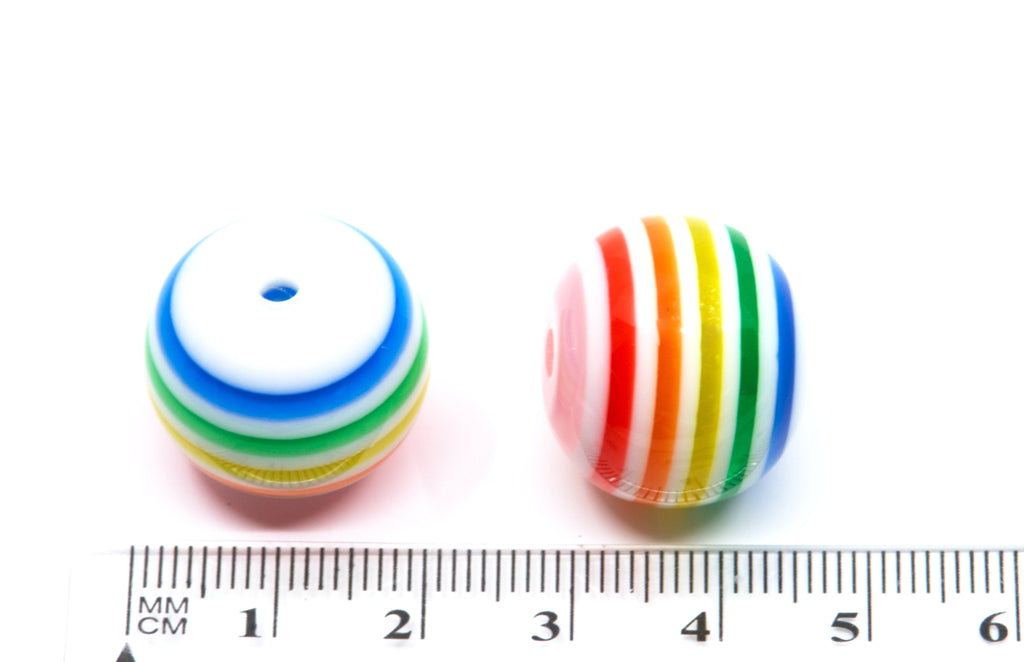 Two rainbow striped bubblegum beads nest to a cm ruler for scale on a white background.