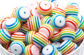 a white ceramic bowl filled with rainbow striped bubblegum beads on a white background 