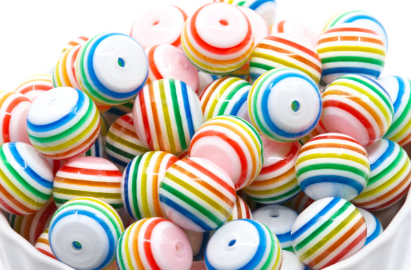 a white ceramic bowl filled with rainbow striped bubblegum beads on a white background 