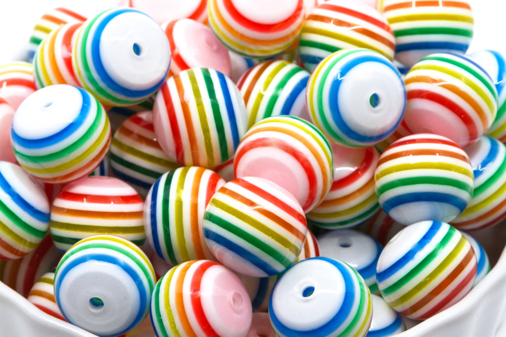 a white ceramic bowl filled with rainbow striped bubblegum beads on a white background 