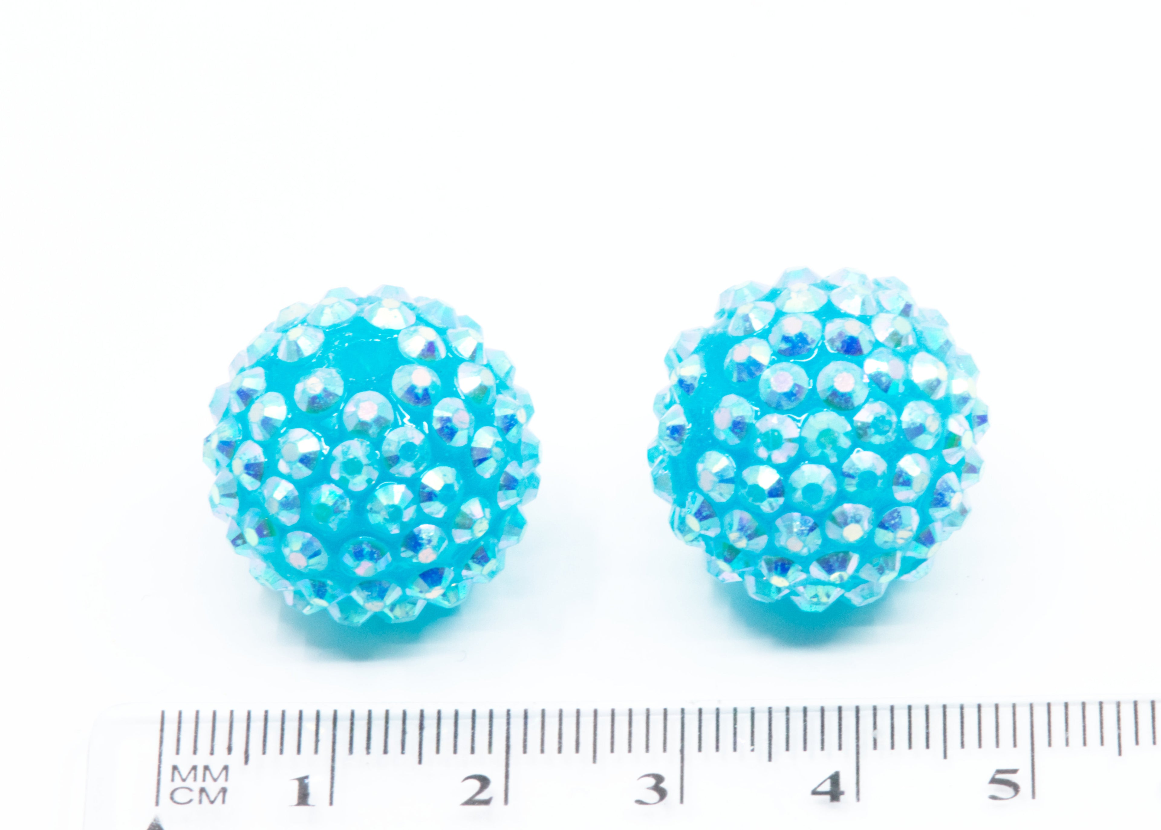 two blue rhinestone beads with a ruler for scale on a white background