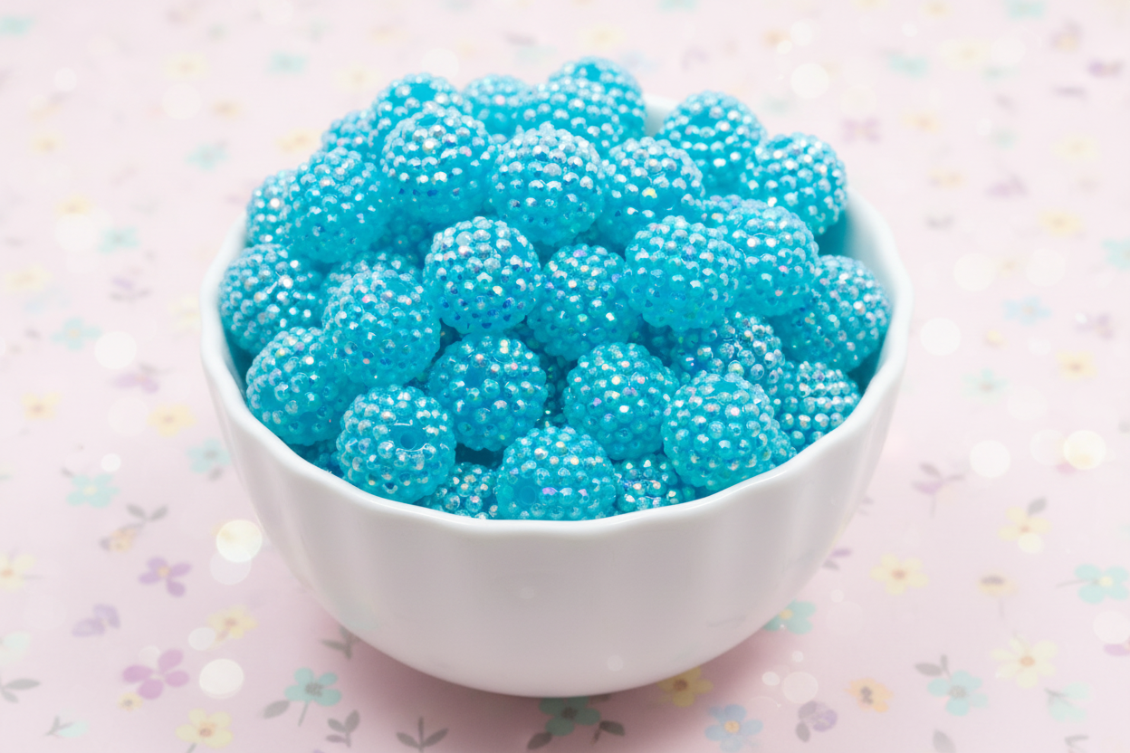 blue rhinestone beads in a white bowl on a light pink background 