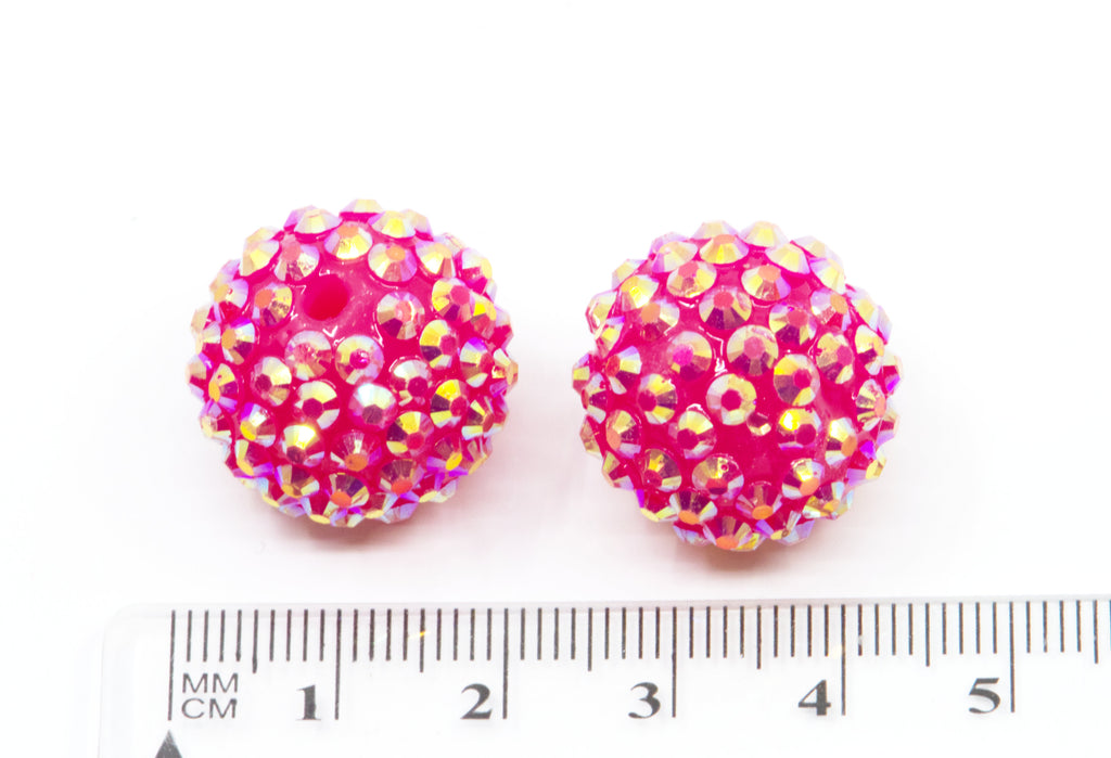Two round pink rhinestone-covered beads shown next to a white ruler for scale on a white background.