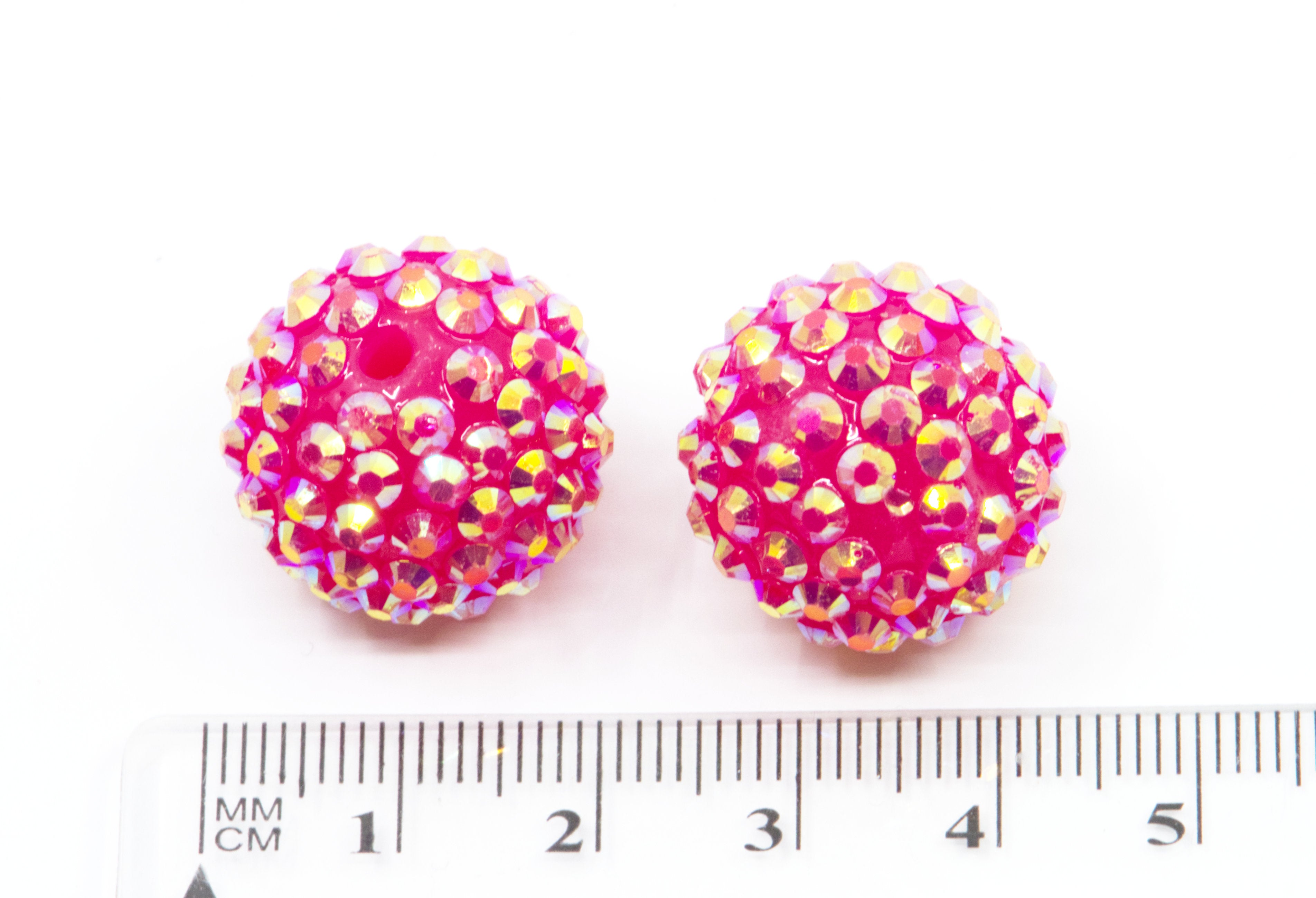Two round pink rhinestone-covered beads shown next to a white ruler for scale on a white background.