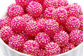 A close-up of bright pink rhinestone-covered round beads or embellishments piled in a white bowl against a white background.