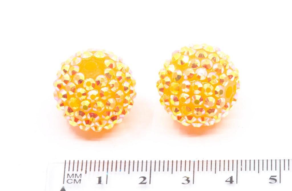 Pair of orange rhinestone beads with a ruler for scale on a white background