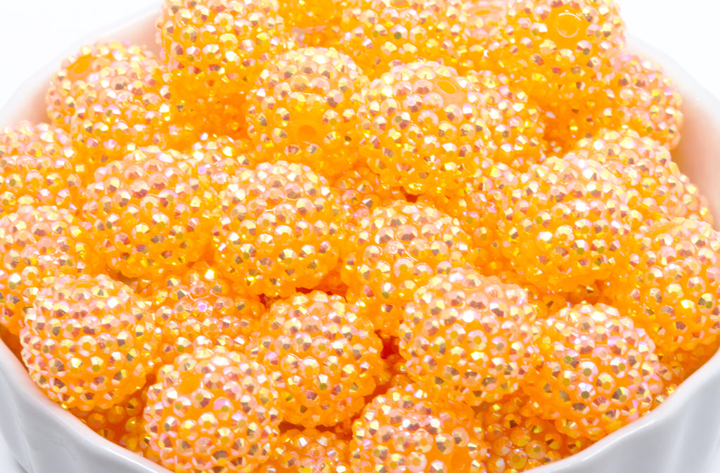 Close-up of orange rhinestone beads in a white bowl with a white background