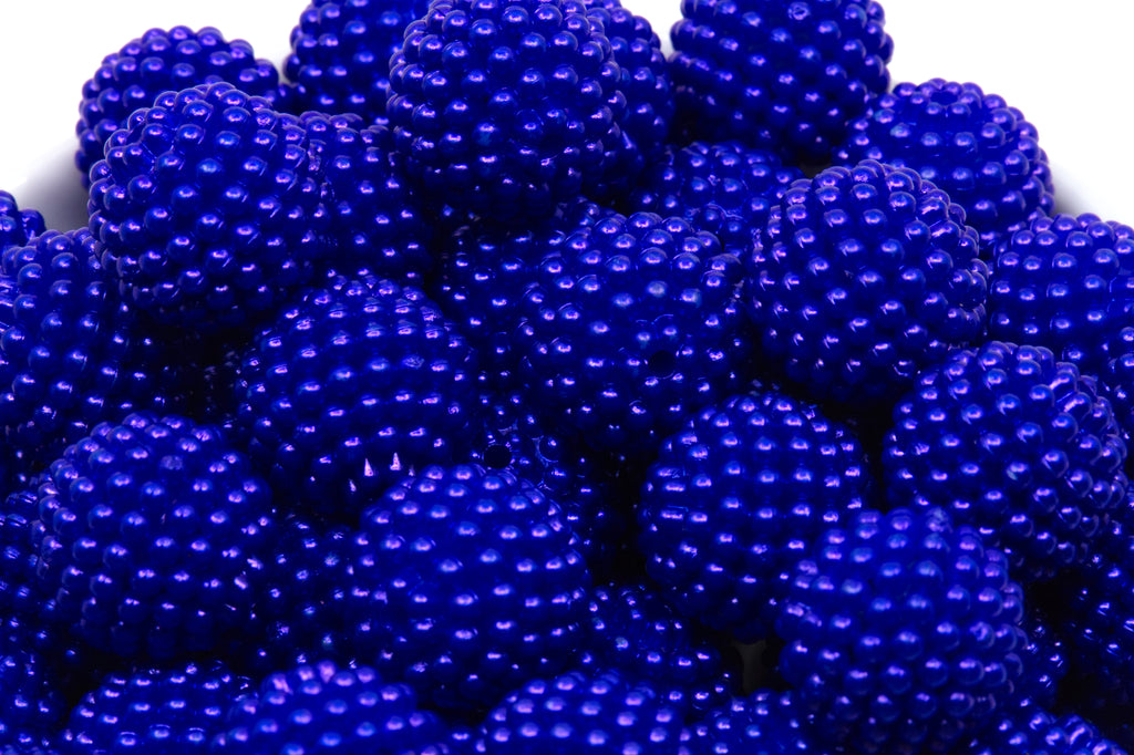 A close-up of blue beaded bubblegum beads piled in a white bowl against a white background.