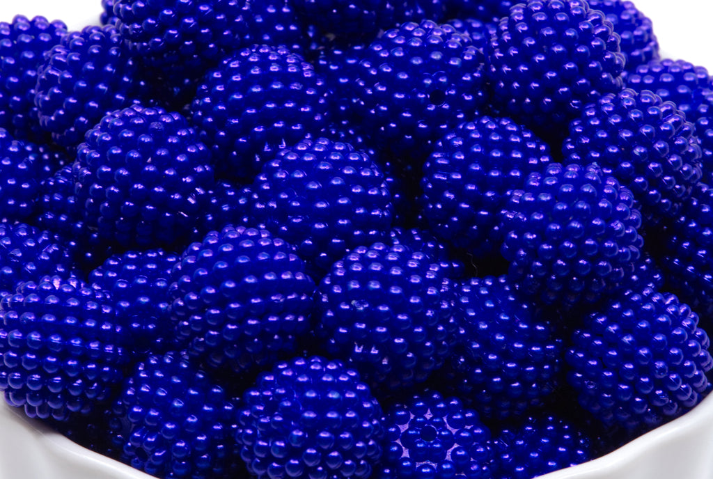 A close-up of blue beaded bubblegum beads piled in a white bowl against a white background.