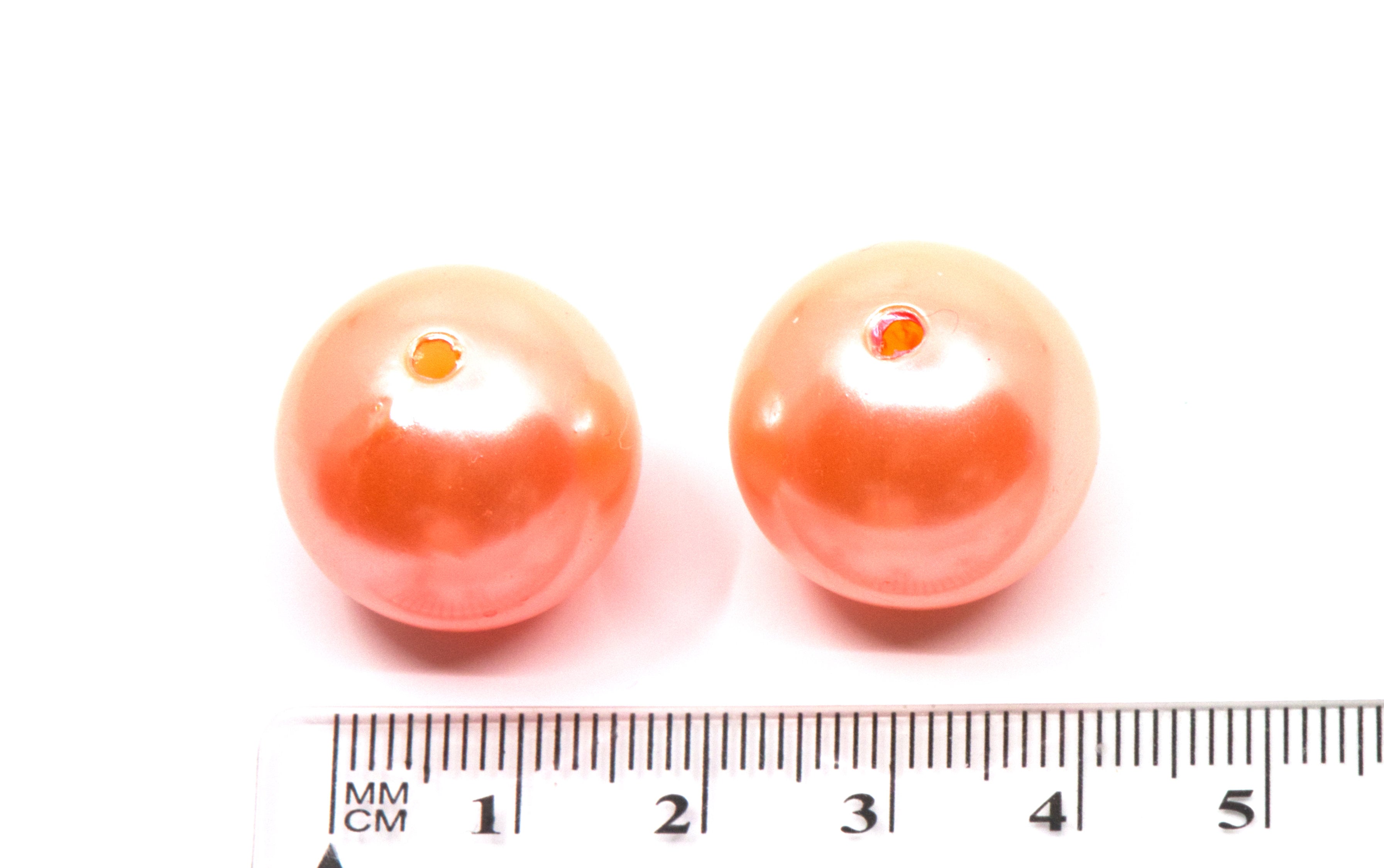 Two round sherbet orange shiny pearl bubblegum beads with central holes, displayed above a  cm ruler to indicate size on a white background.