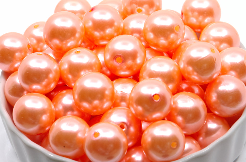A pile of shiny sherbet orange round shiny pearl beads with center holes, shown in a white bowl against a white background.