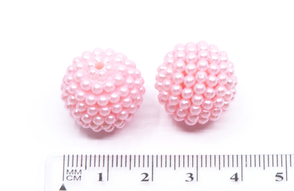 two pink bubblegum beads next to ruler for scale on a white background