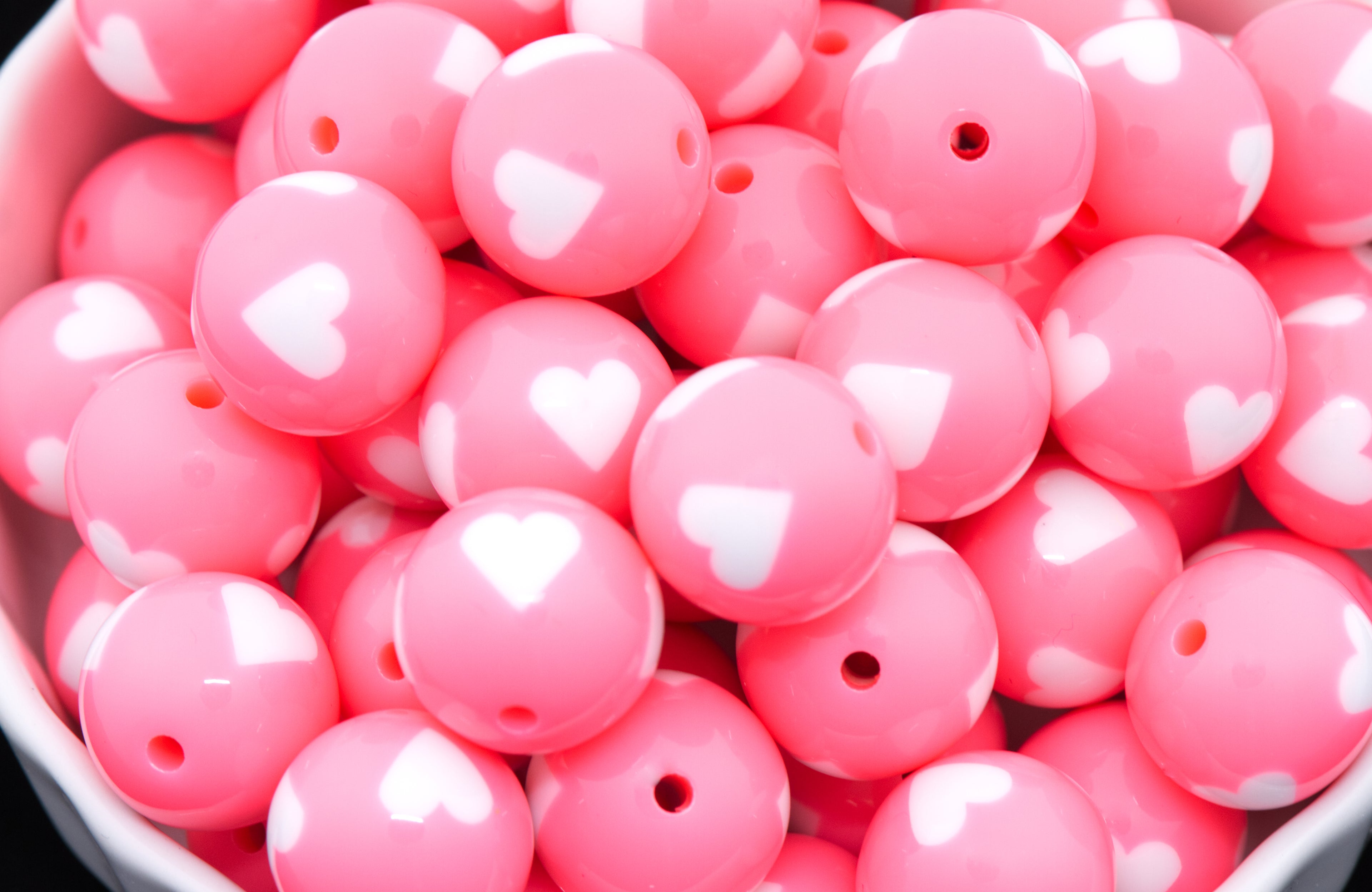 Pink beads with white heart patterns in a bowl