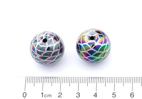 Two round iridescent beads with a mermaid scale pattern next to a cm ruler on a white background. 