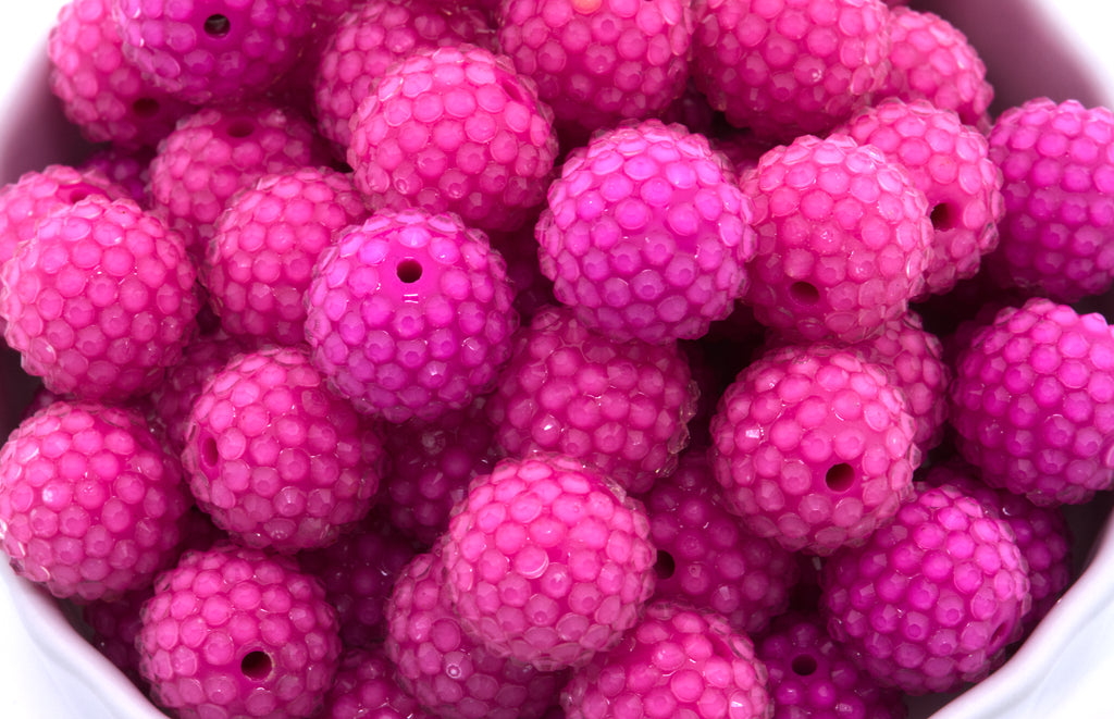 A close-up of bright rhinestone bubblegum beads piled inside a white bowl on a white background. 