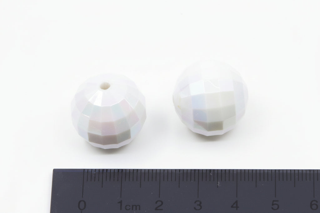 Two faceted white beads on a white background with a ruler for scale.