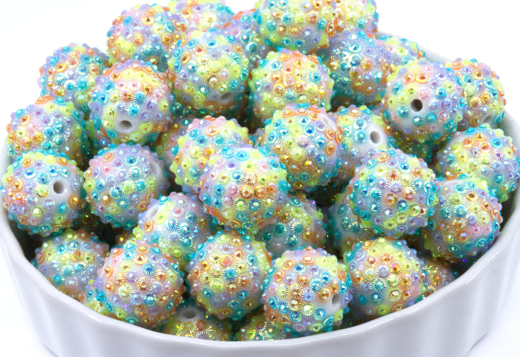 rainbow rhinestone beads in a white bowl on a white background 