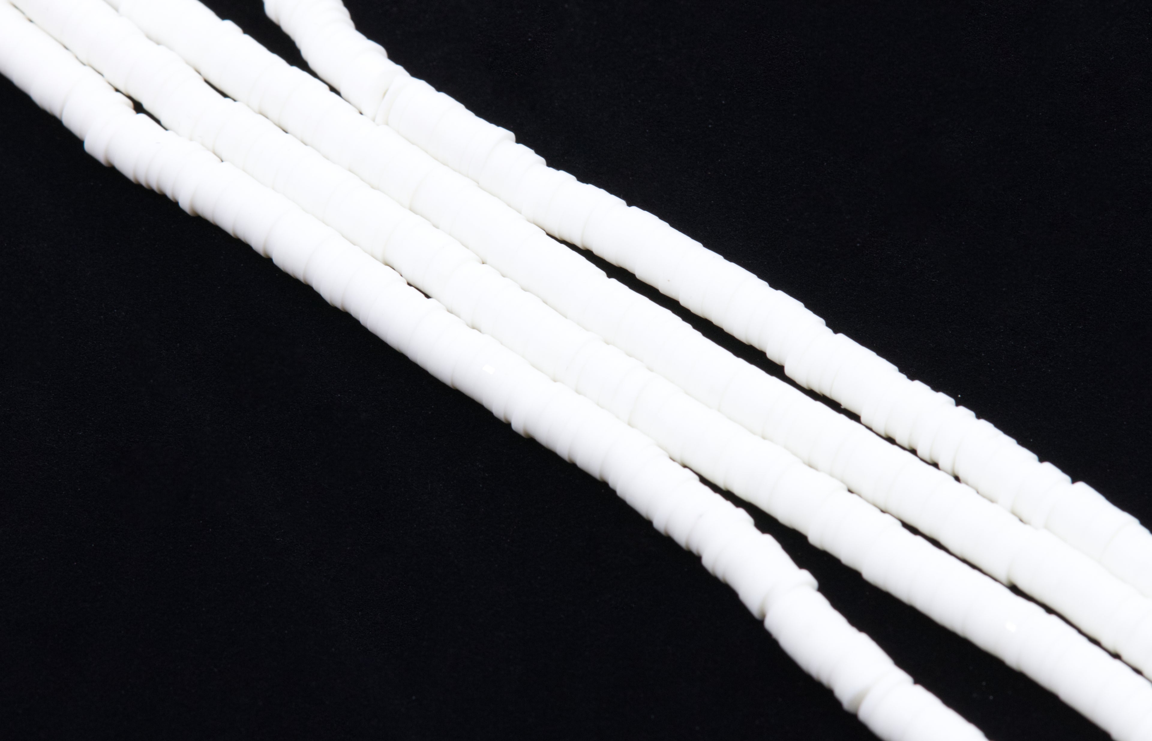 multiple strands of white polymer clay disc beads arranged diagonally on a solid black background.