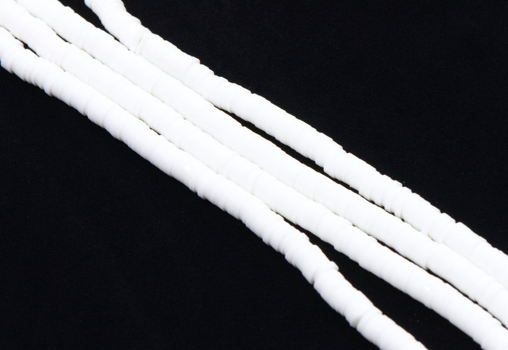 multiple strands of white polymer clay disc beads arranged diagonally on a solid black background.