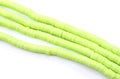 multiples strands of light green, polymer clay disc beads arranged diagonally on a plain white background.