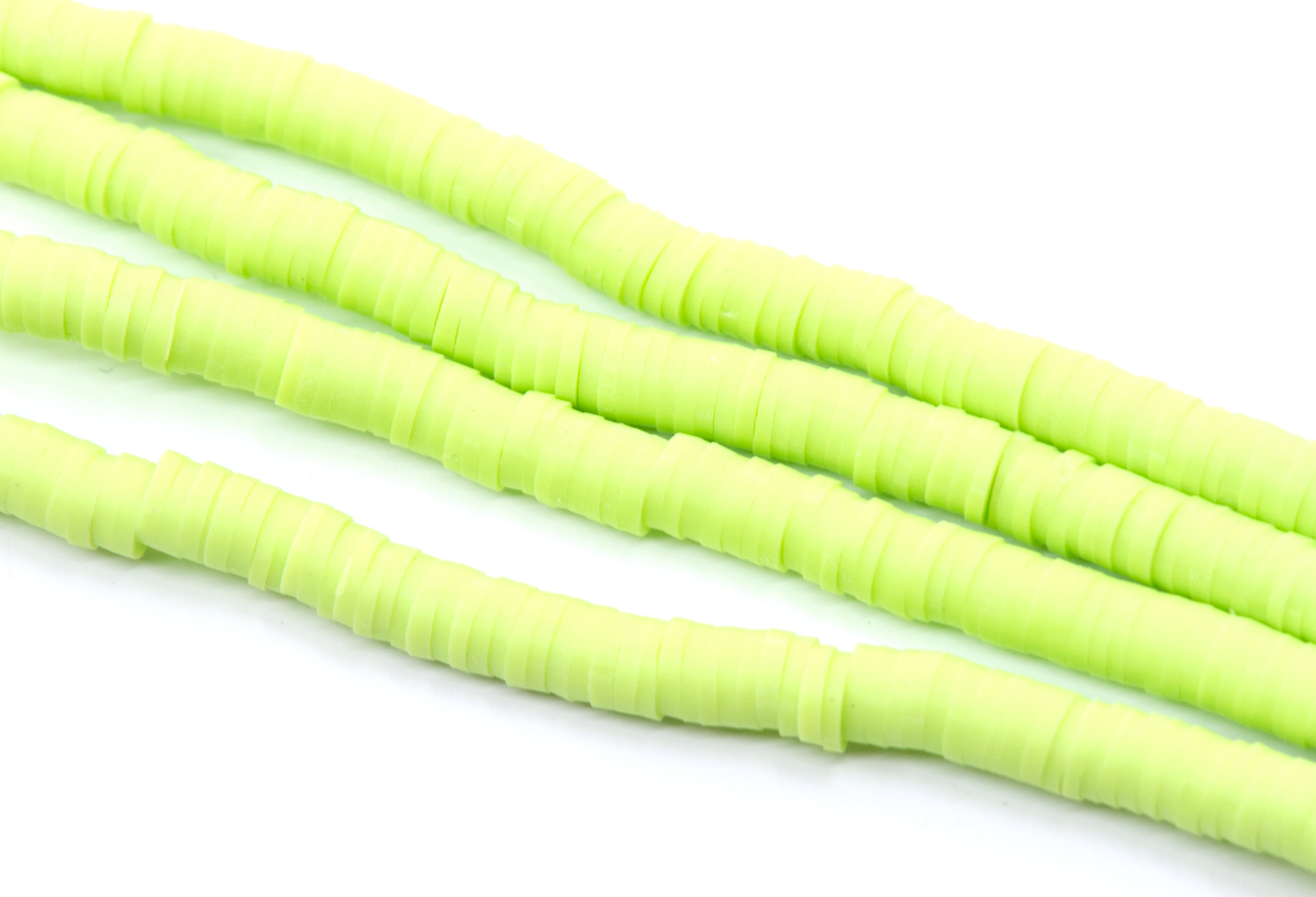 multiples strands of light green, polymer clay disc beads arranged diagonally on a plain white background.