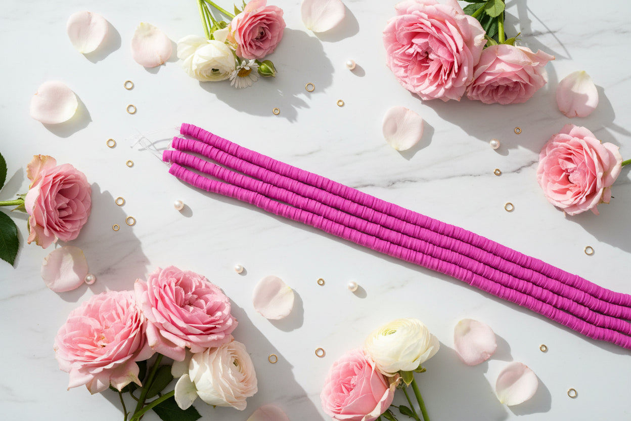 Bright pink polymer clay beads arranged in diagonal strands on a white background with pink roses