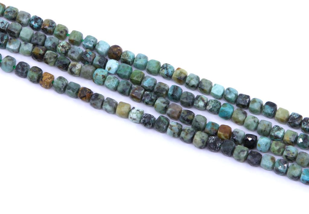 four strands of African turquoise faceted, cube gemstone beads in earthy green, blue, brown, and black marbled patterns, laid diagonally on a white background.