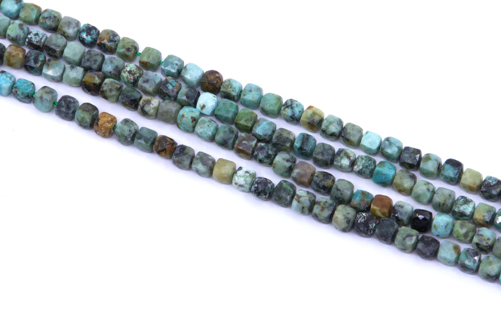 four strands of African turquoise faceted, cube gemstone beads in earthy green, blue, brown, and black marbled patterns, laid diagonally on a white background.