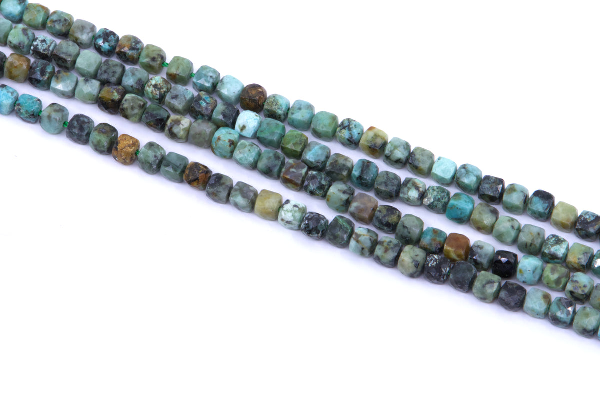 four strands of African turquoise faceted, cube gemstone beads in earthy green, blue, brown, and black marbled patterns, laid diagonally on a white background.
