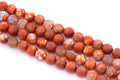 Four strands of round faceted agate beads in a mottled orange, and white agate pattern, arranged diagonally on a white background.