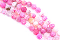 Pink faceted agate beads arranged in diagonal strands on a white background.