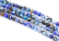 Multiple strands of faceted agate beads in shades of blue,  black, and white  arranged diagonally on a plain white background.