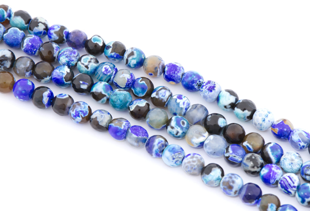 Multiple strands of faceted agate beads in shades of blue,  black, and white  arranged diagonally on a plain white background.