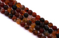 Faceted round beads in a mix of translucent amber, deep red, and dark black-brown tones, arranged diagonally on a plain white background.