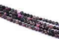Faceted round agate beads on strands, featuring a pink and black coloring, displayed on a clean white background.