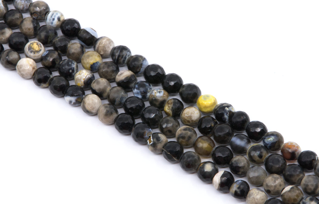 Multiple strands of polished faceted round gemstone beads in black, gray, brown, and white , arranged diagonally on a white background.