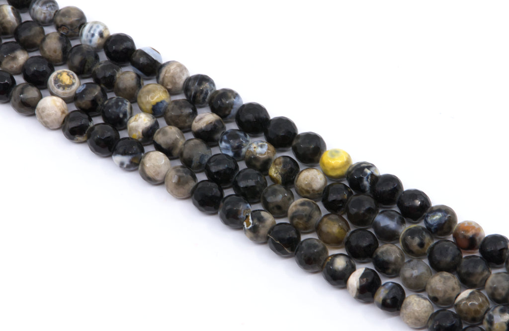 Multiple strands of polished faceted round gemstone beads in black, gray, brown, and white , arranged diagonally on a white background.